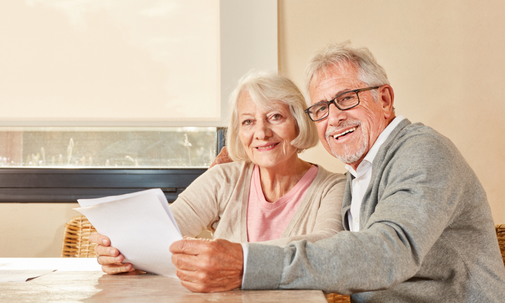 Senior husband and wife holding papers looking at the camera, smiling